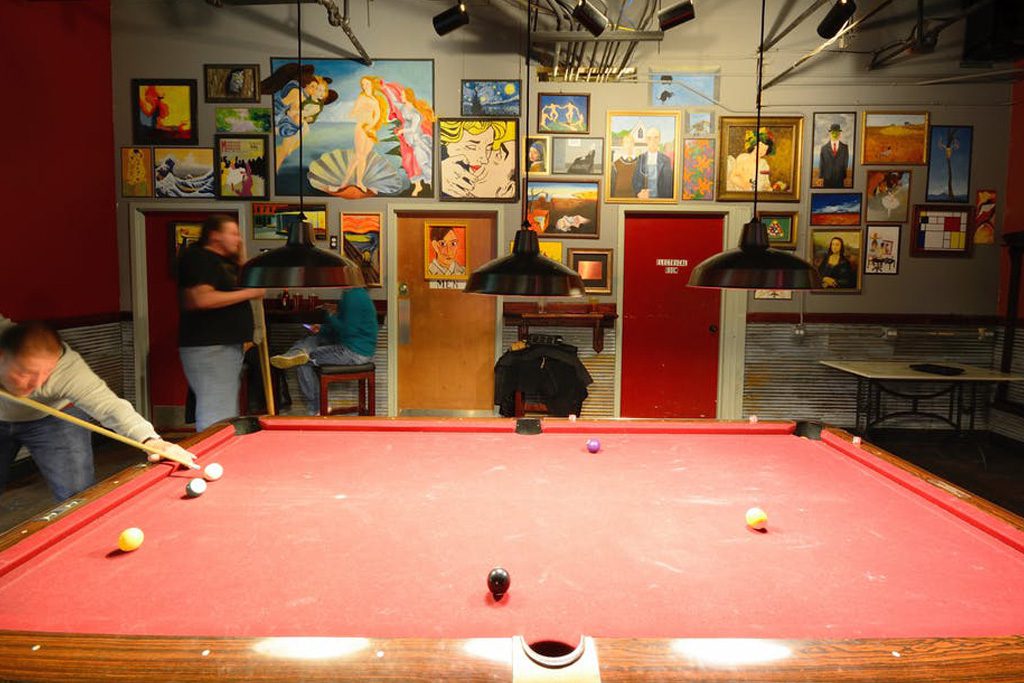 guests playing billiards with a red table and pop paintings